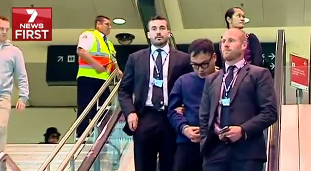 Detectives escort the latest man arrested through the airport at Sydney. Photo: 7 News