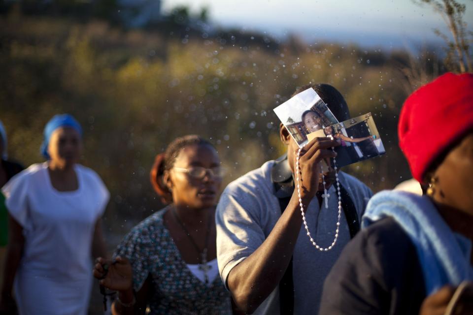 In this Feb. 8, 2014 photo, Christian pilgrims holding a rosary and photographs is sprinkled in holy water during a religious gathering in the village of Bois-Neuf, Haiti. Some brought photos of sick family members in hopes that their prayers will rid them of illness. (AP Photo/Dieu Nalio Chery)