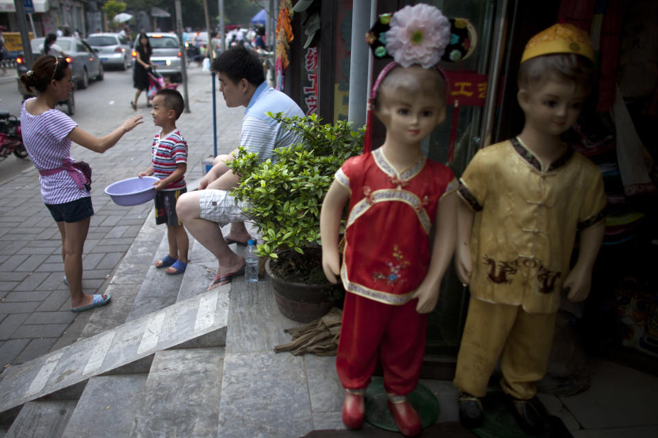 In this Sunday, July 8, 2012 photo, a family chat outside their souvenir shop in a hutong, an old alleyway, near the Houhai lake in Beijing, China. To see a side of Beijing other than glitzy shopping malls or imposing, Soviet-style government buildings, take an afternoon to explore the city's ancient narrow alleyways, known as hutongs. (AP Photo/Alexander F. Yuan)