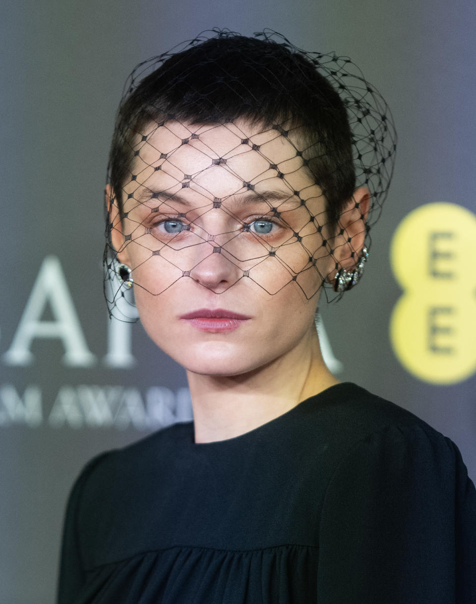 Emma Corrin wears a black dress with a netted headpiece at an event