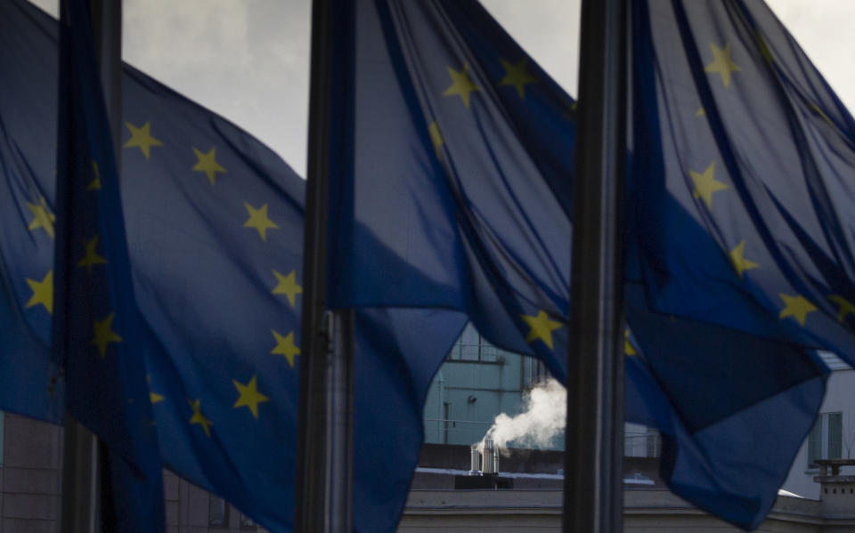 Smoke rises from a chimney behind EU flags fluttering in the wind outside EU headquarters in Brussels, Thursday, Dec. 24, 2020. European Union and British negotiators worked through the night and into Christmas Eve in the hopes of putting the finishing touches on a trade deal that should avert a chaotic economic break between the two sides on New Year's Day. (AP Photo/Virginia Mayo)