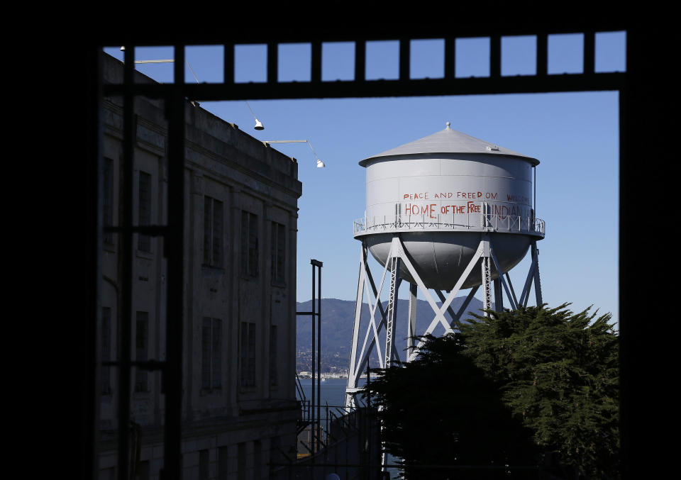 FILE - This Jan. 14, 2013, file photo, shows a restored water tower with words that read "Peace and Freedom Welcome Home of the Free Indian Land" seen through an entryway to the main cell house on Alcatraz Island in San Francisco. The words were first written on the water tower during the Native American occupation. The week of Nov. 18, 2019, marks 50 years since the beginning of a months-long Native American occupation at Alcatraz Island in the San Francisco Bay. (AP Photo/Eric Risberg, File)