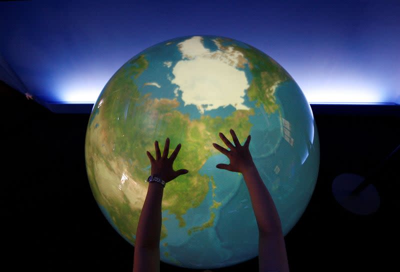 FILE PHOTO: A visitor places her hands on a tangible earth, a digital globe, at an exhibition pavillion in Rusutsu town, northern Japan