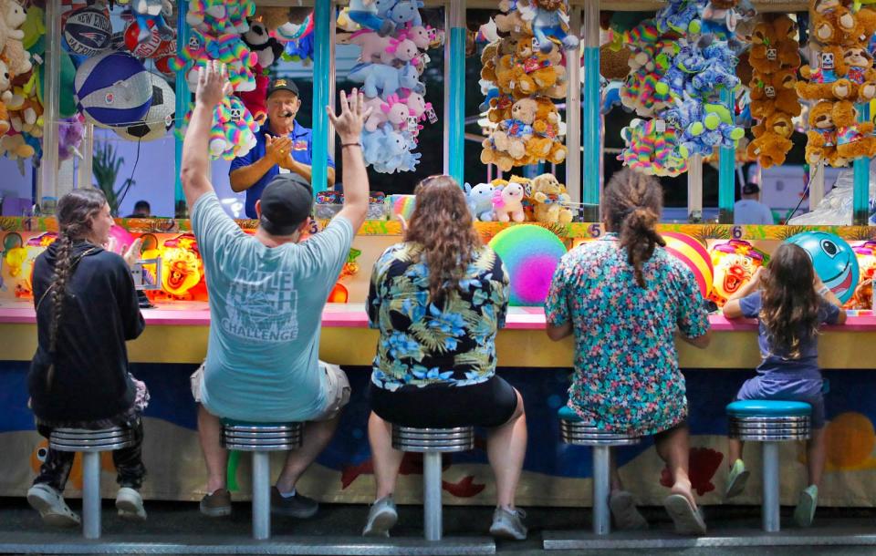 A father raises his hands in victory after winning a water gun game run by carny Larry Creed at the Marshfield Fair on Monday, Aug. 21, 2023.