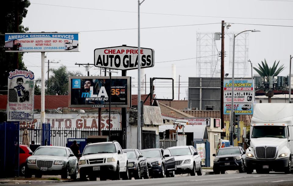 Crowded shops along a city street with signs including "Cheap Price Auto Glass" and "Locksmith."