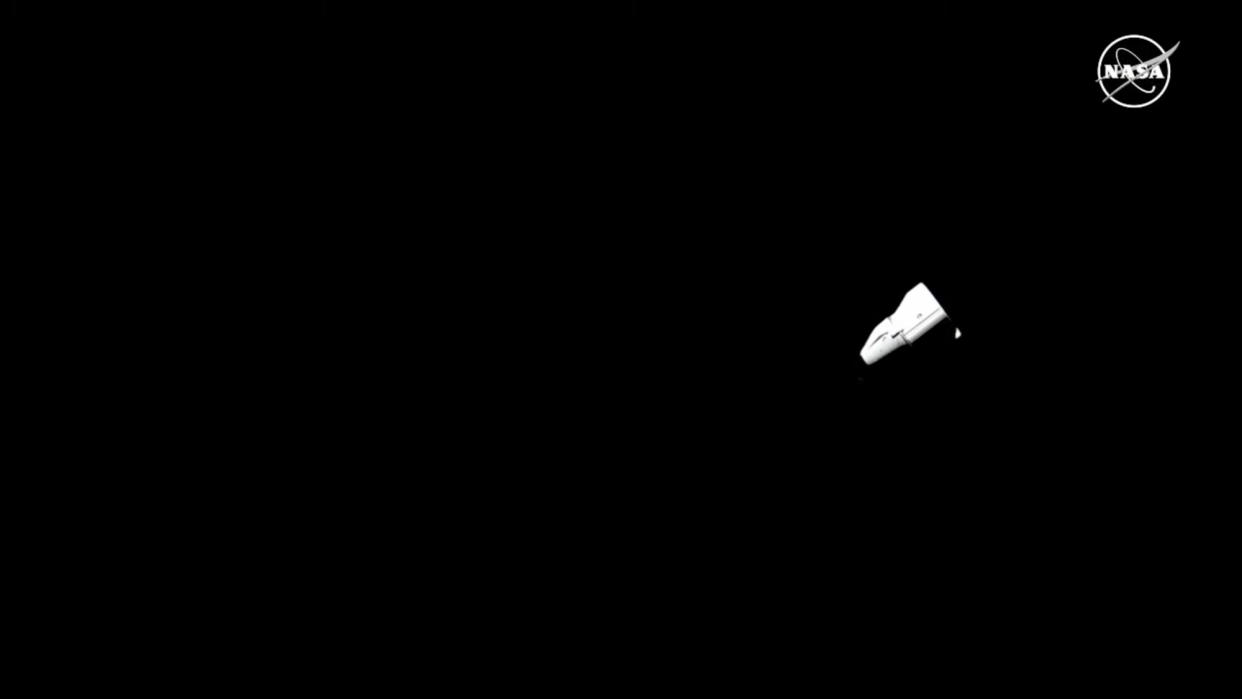  Long-distance view of a conical white capsule against the blackness of space. 