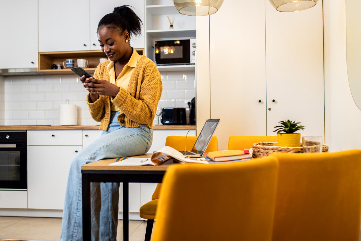 Young African American woman working from her living room using smartphone.