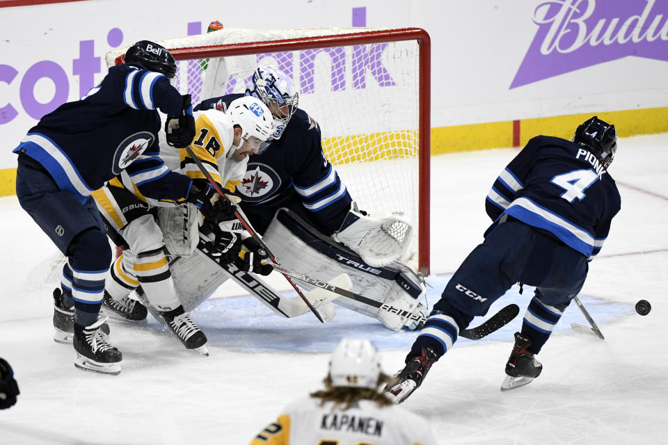 Winnipeg Jets' Neal Pionk (4) clears the rebound after goaltender Connor Hellebuyck (37) made a save on Pittsburgh Penguins' Jason Zucker (16) during the second period of an NHL hockey game Monday, Nov. 22, 2021, in Winnipeg, Manitoba. (Fred Greenslade/The Canadian Press via AP)