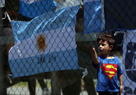 A boy stands next to an Argentine national flag with a message in support of the 44 crew members of the missing at sea ARA San Juan submarine outside an Argentine naval base in Mar del Plata, Argentina November 25, 2017. Words on the flag read "ARA San Juan, we wait for you". REUTERS/Marcos Brindicci