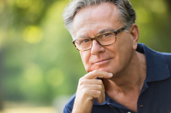 A senior man in deep thought, with his chin resting on his right hand.