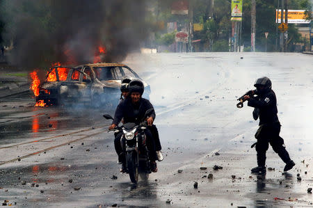 FILE PHOTO: A riot police officer fires his shotgun towards two men during a protest against Nicaragua's President Daniel Ortega's government in Managua, Nicaragua May 28, 2018. REUTERS/Oswaldo Rivas/File Photo
