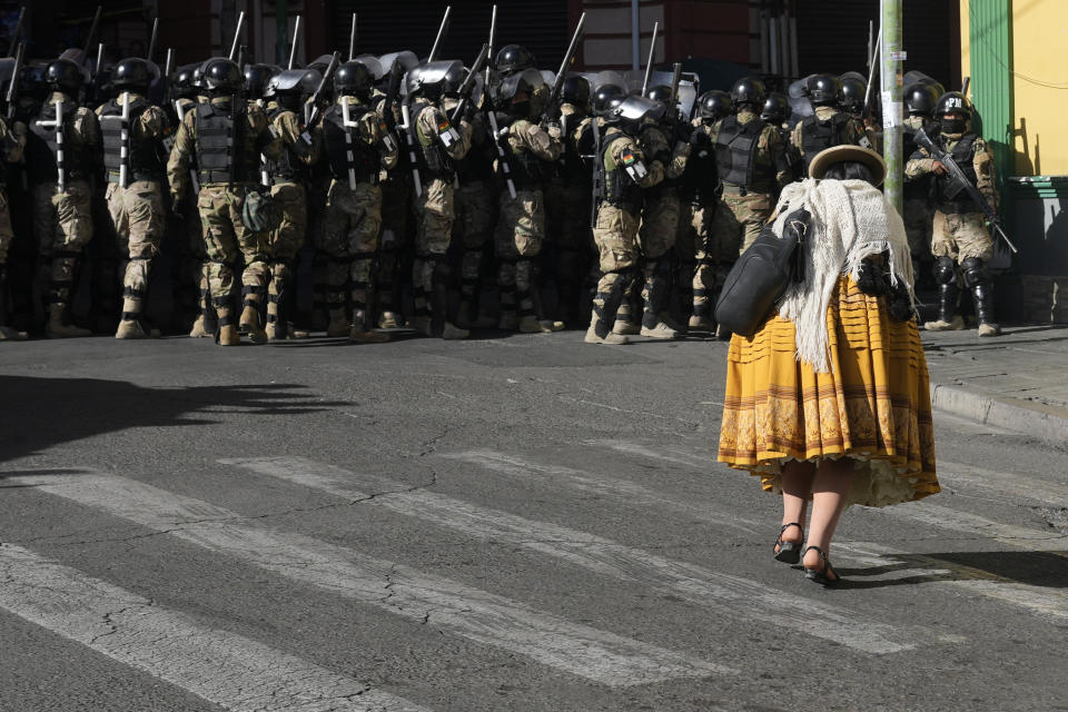 A woman walks by military police in Plaza Murillo, in La Paz, Bolivia, Wednesday, June 26, 2024. Armored vehicles rammed into the doors of Bolivia's government palace located in Plaza Murillo, on Wednesday as President Luis Arce said the country faced an attempted coup. (AP Photo/Juan Karita)