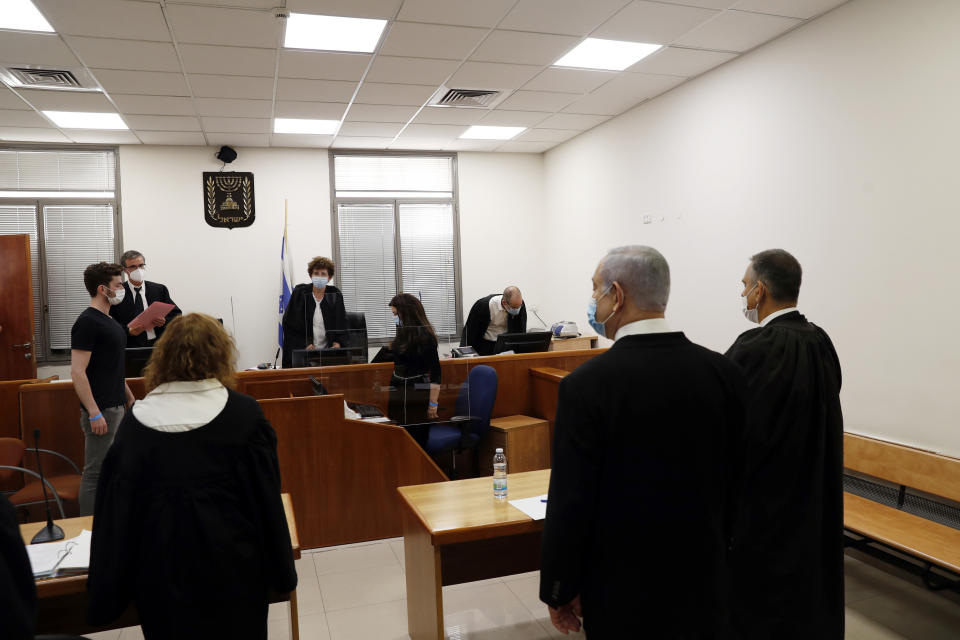 Israeli Prime Minister Benjamin Netanyahu, second right, stands while the judges enter the court room as his corruption trial opens at the Jerusalem District Court, Sunday, May 24, 2020. He is the country’s first sitting prime minister ever to go on trial, facing charges of fraud, breach of trust, and accepting bribes in a series of corruption cases stemming from ties to wealthy friends. (Ronen Zvulun/ Pool Photo via AP)
