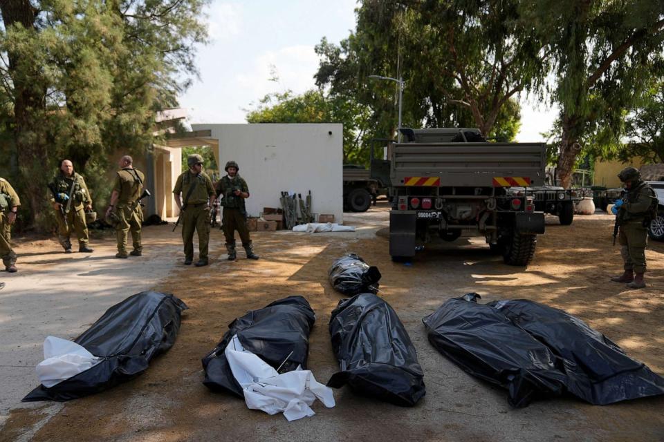 PHOTO: Israeli soldiers stand next to the bodies of Israelis killed by Hamas militants in kibbutz Kfar Azza on Oct. 10, 2023. (Ohad Zwigenberg/AP)