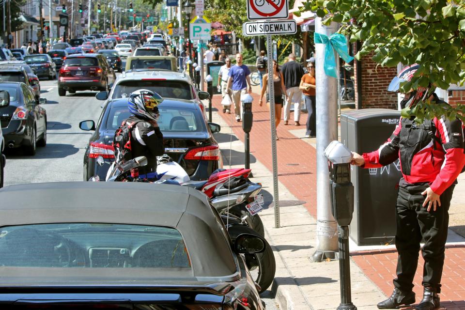 A motorcyclist pays a parking meter as traffic streams by on Main Street in Newark, Del.