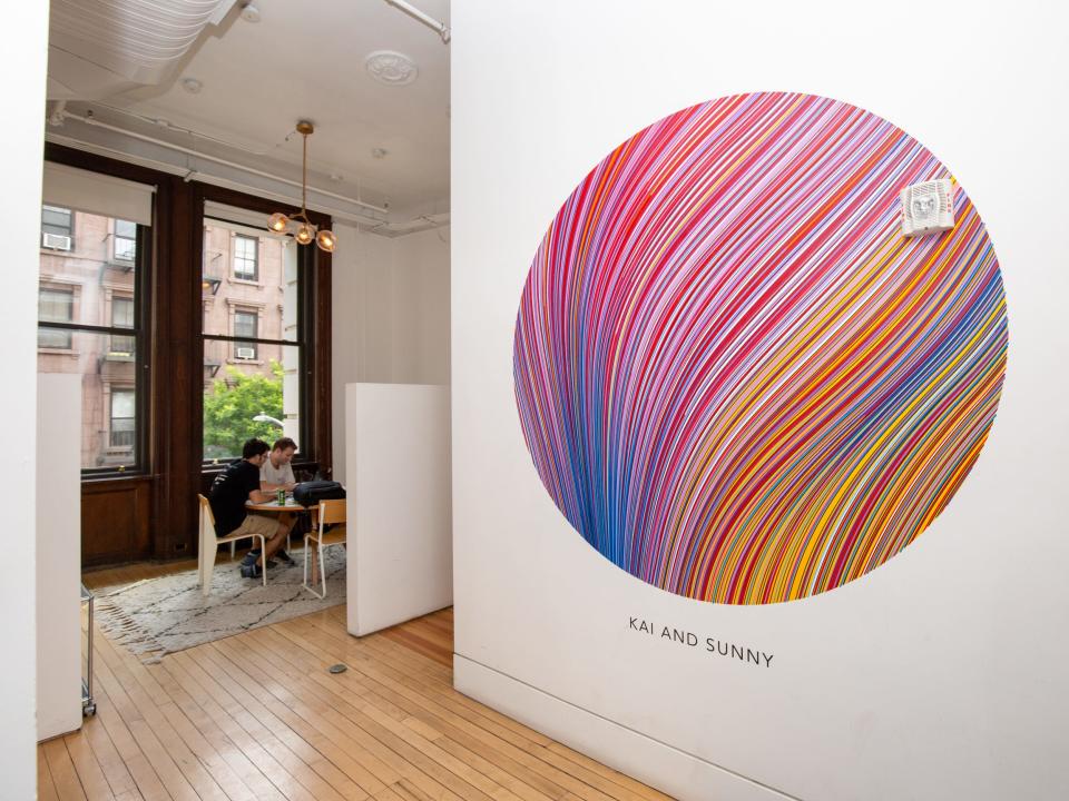 A wall with a colorful circular design. Two people are working at a table nearby.