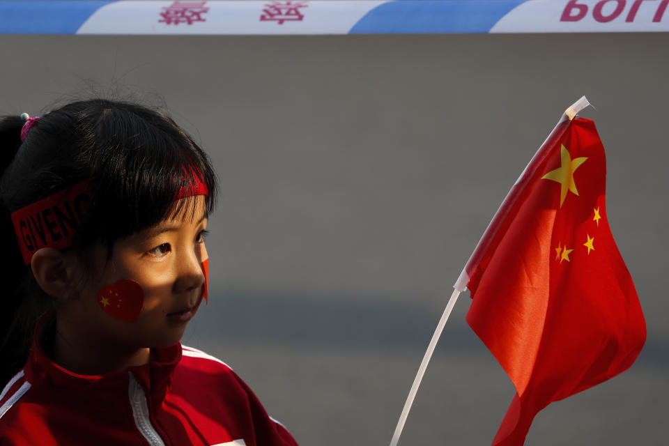 A child waves a national flag behind a police barricade line as residents watch Chinese military vehicles and floats in preparation for the parade for the 70th anniversary of the founding of the People's Republic of China, in Beijing, Tuesday, Oct. 1, 2019. (AP Photo/Andy Wong)