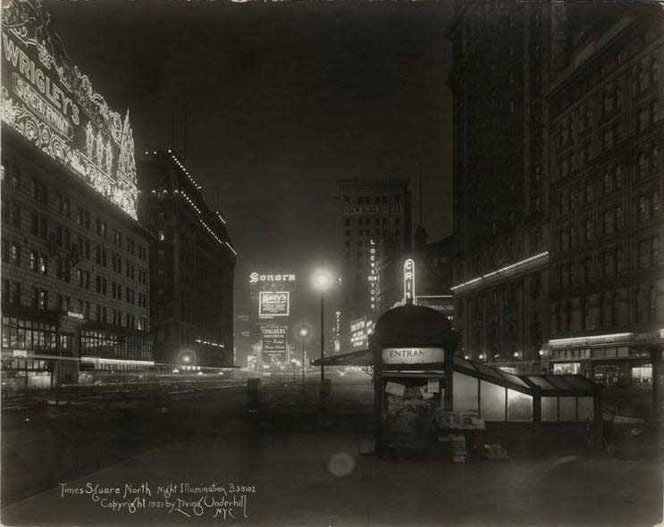 Times Square illuminated at night in 1921, subway station visible in foreground.