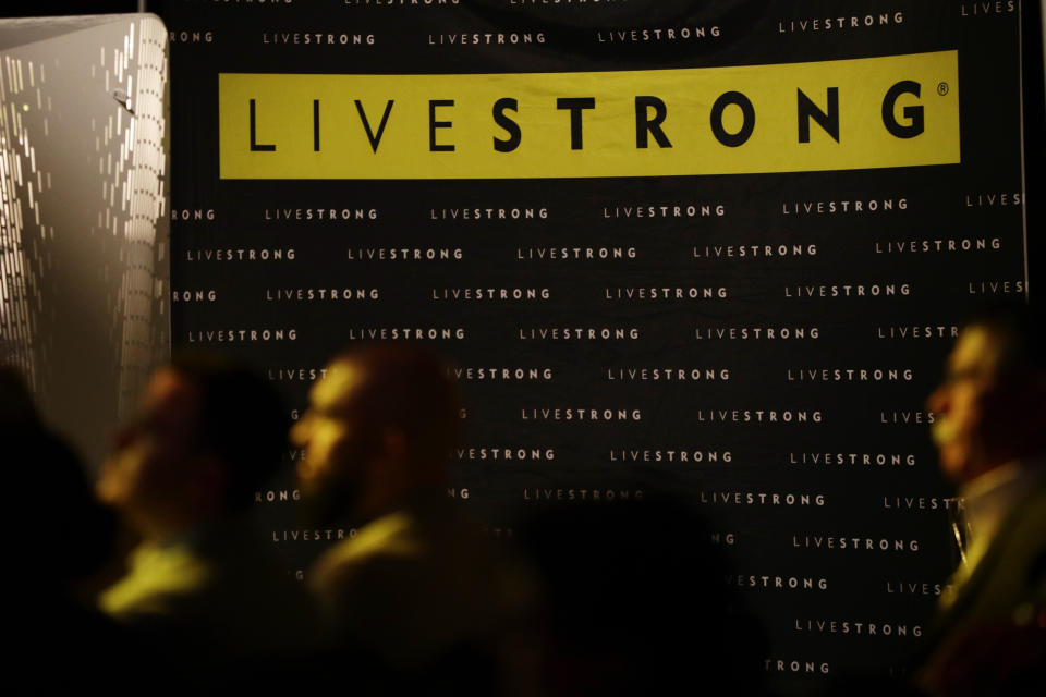 In this Monday, Feb. 3, 2020 photo, guests sit near the old logo for Livestrong at an event in Austin, Texas. The Livestrong cancer charity is on a mission to reinvent itself. It has survived a dramatic fall in contributions and donations since founder Lance Armstrong's performance-enhancing drug scandal. (AP Photo/Eric Gay)