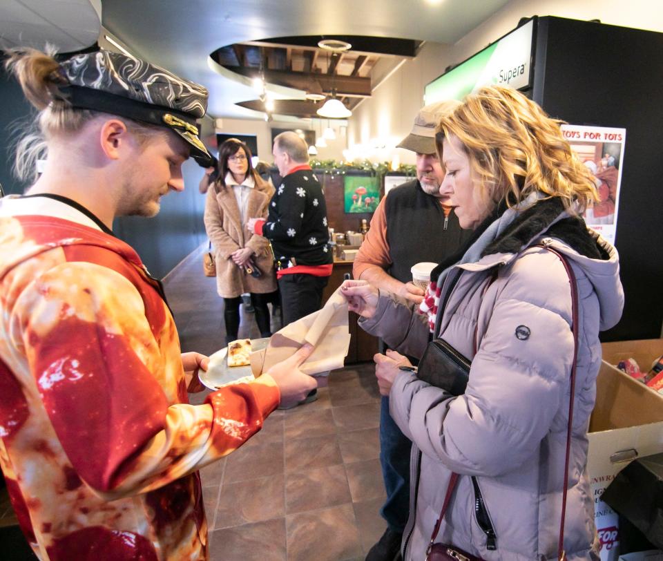 Owner Nick Mannisto hands out roasted garlic cheese bread to Brighton residents Steven and Mary Beth Potrykus at the grand opening of Captain's on Main in downtown Brighton Friday, Nov. 18, 2022.