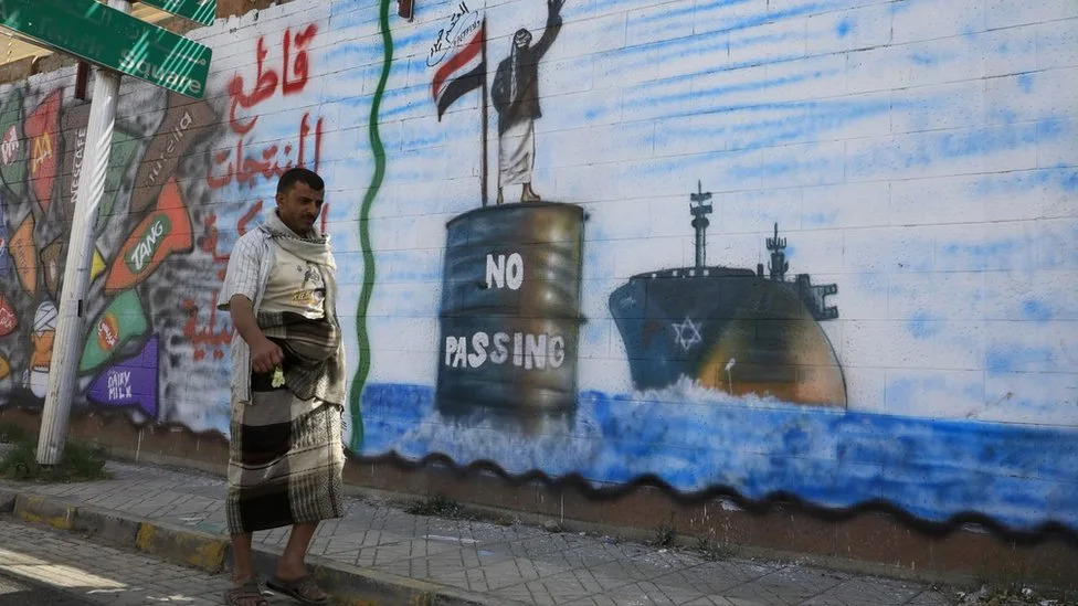 A Yemeni man walks past a mural showing a Houthi fighter stopping an Israeli ship in the Red Sea, in Sanaa, Yemen (19 February 2024)