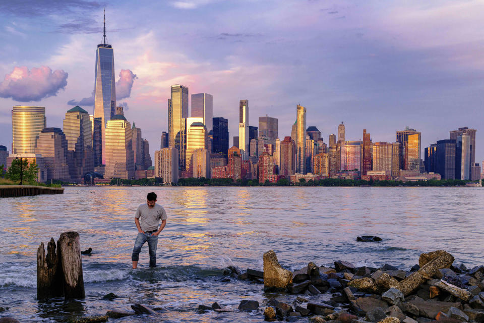 A man checks his footing as he wades through the Morris Canal Outlet in Jersey City, N.J., as the sun sets on the lower Manhattan skyline of New York City, Tuesday, May 31, 2022. (AP Photo/J. David Ake)