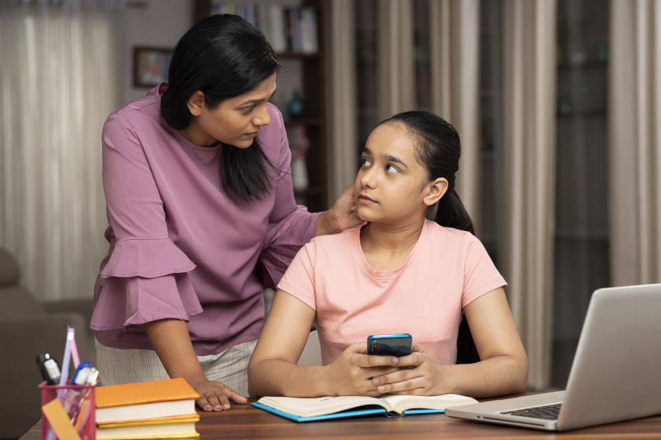 Woman consoling teenage girl with laptop and book on table, expressing concern and comfort