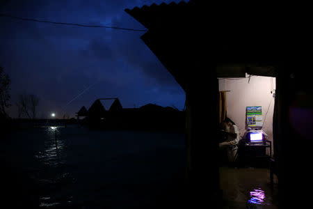 A girl uses her smartphone as high tide floods her house at Sriwulan village in Demak, Indonesia, January 30, 2018.