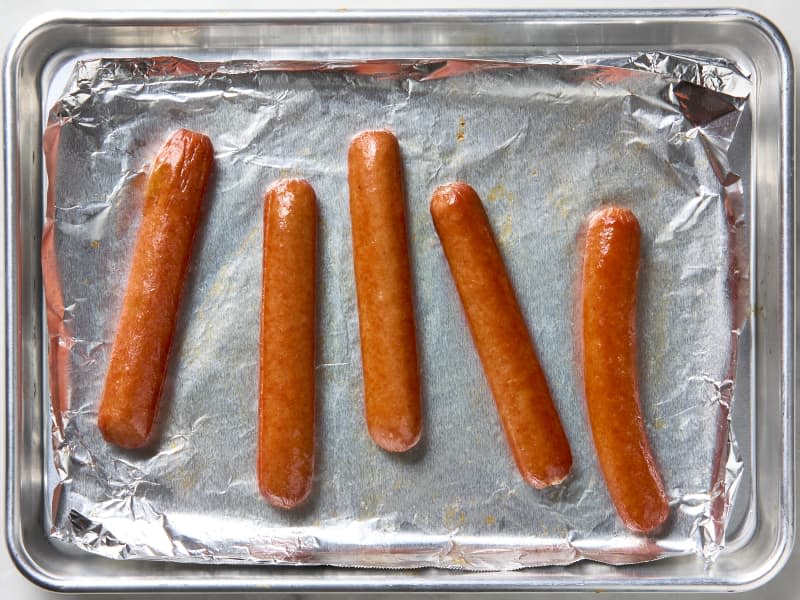 overhead photo of hot dogs cooked in under the broiler on a foil lined sheet pan