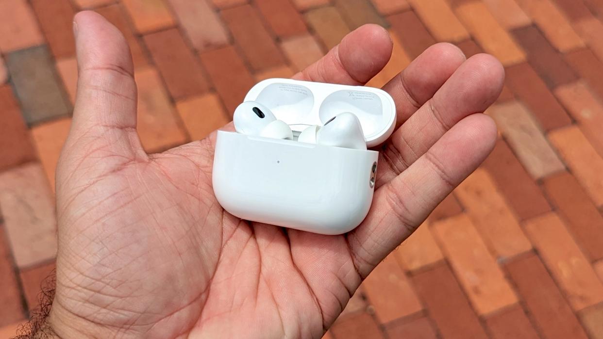  AirPods Pro 2 in charging case in reviewer's hand with red brick paving in background 