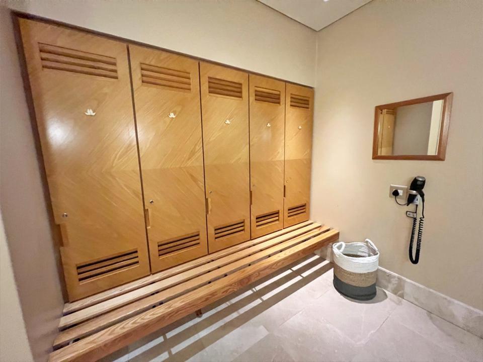 Locker room with wooden lockers, a wooden bench, a fabric hamper, and a blow dryer on the wall