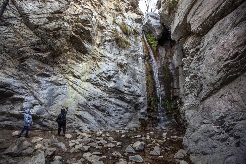 A person points at a waterfall in a rocky canyon