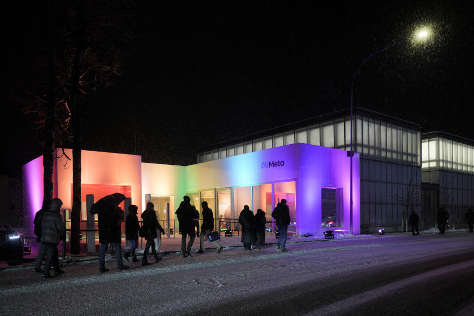 People walk in front of the in rainbow colours illuminated building of the Meta company on Promenadenstrasse street, during the World Economic Forum in Davos, Switzerland, Wednesday, Jan. 18, 2023. The annual meeting of the World Economic Forum is taking place in Davos from Jan. 16 until Jan. 20, 2023. (AP Photo/Markus Schreiber)
