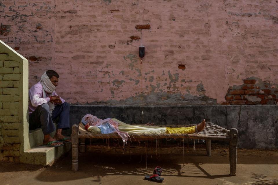 A man sits next to his wife, who was suffering from a high fever, as she intravenously receives rehydration fluid at a makeshift clinic in Parsaul village, Uttar Pradesh on 22 May 2021 (Reuters/Adnan Abidi)