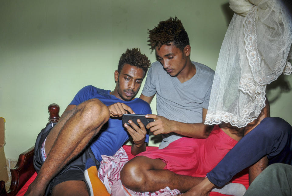 In this photo taken Thursday, Oct. 10, 2019, Eritrean under-20 soccer players Mewael Tesfai Yosief, left, and Simon Asmelash Mekonen look at a smartphone in a house where they are staying in Uganda. Four young players with Eritrea's national under-20 soccer team have defected during a tournament in Uganda, the latest players to leave one of the world's most tightly controlled regimes. (AP Photo)