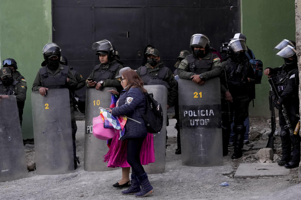 Women walk past police in riot police guarding the police facility where Luis Fernando Camacho, governor of Santa Cruz, is kept in custody in La Paz, Bolivia, Thursday, Dec. 29, 2022. Camacho, the country's main opposition leader, was arrested Wednesday on terrorism charges. (AP Photo/Juan Karita)