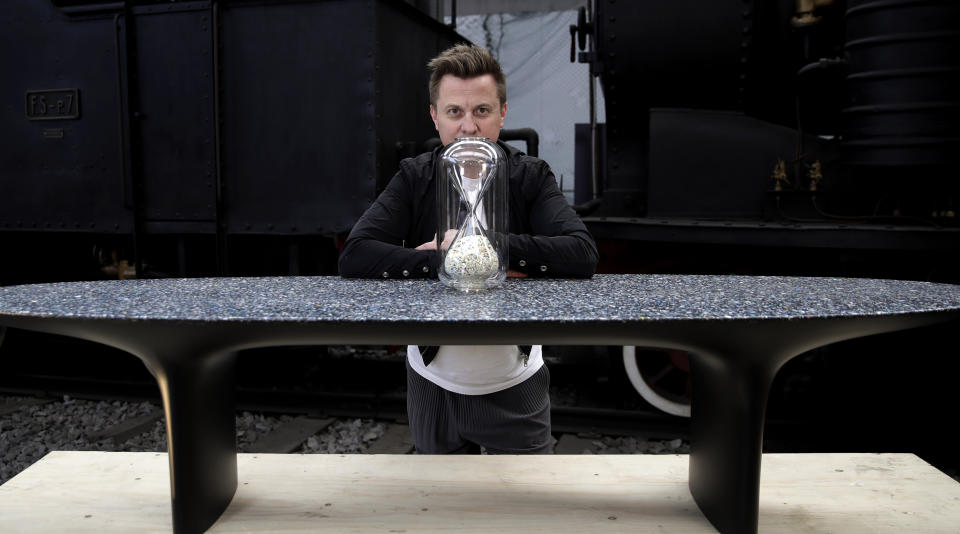 In this picture taken on Saturday, April 13, 2019, Australian designer Brodie Neill poses next to his creation '"Capsule: Ocean Plastic Hourglass", on a table made with his self-created Ocean Terrazzo material, made with plastic waste from oceans, at the National Museum of Science and Technology, during the "RO Plastic - Master's Pieces" exhibition', on the sidelines of the Salone del Mobile International Furniture Fair week, in Milan, Italy. Scientists and environmental activists have been long raised the alarm on plastic pollution. Now, the high-end design world is getting in on the growing global effort to tackle plastic pollution -- by upcycling discarded objects into desirable one-off design pieces. (AP Photo/Luca Bruno)