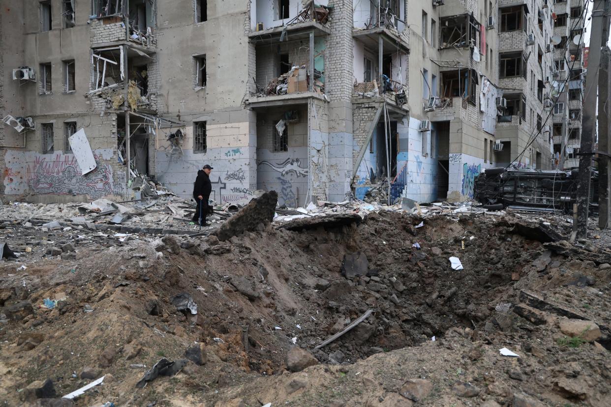 A local resident passes by a crater caused by a Russian rocket attack, which hit several buildings in central Kharkiv (AP)