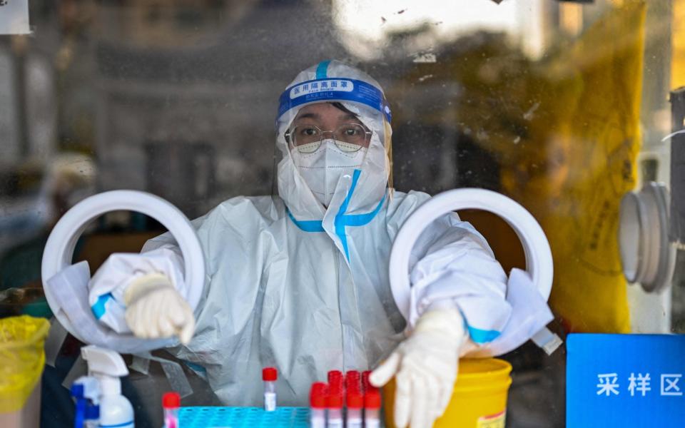 A health worker waits for people to take swab samples to test for Covid-19 in Shanghai - Hector Retamal/AFP