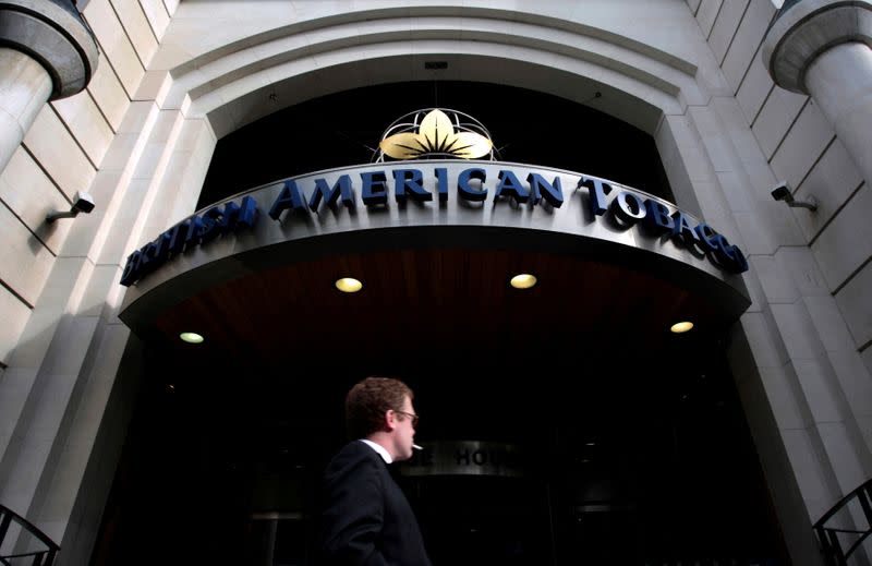 FILE PHOTO: A man smokes as he passes the British American Tobacco offices in London