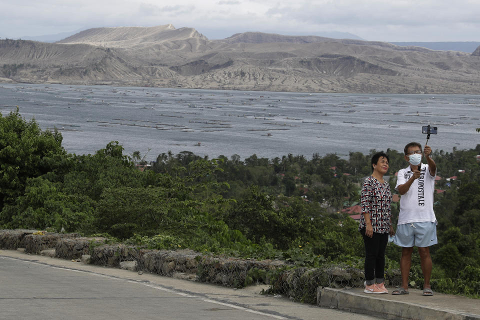 A couple poses for a selfie with the Taal volcano in background almost a year after it erupted on Sunday, Jan. 10, 2021 in Batangas province, Philippines. A popular tourist destination just south of Manila because of its picturesque setting in the middle of a lake, Taal erupted on Jan. 12, 2020. The eruption displaced thousands of villagers living near the area and delivered an early crisis this year for one of the world's most disaster-prone nations a couple of months before the COVID-19 pandemic broke in the country. (AP Photo/Aaron Favila)