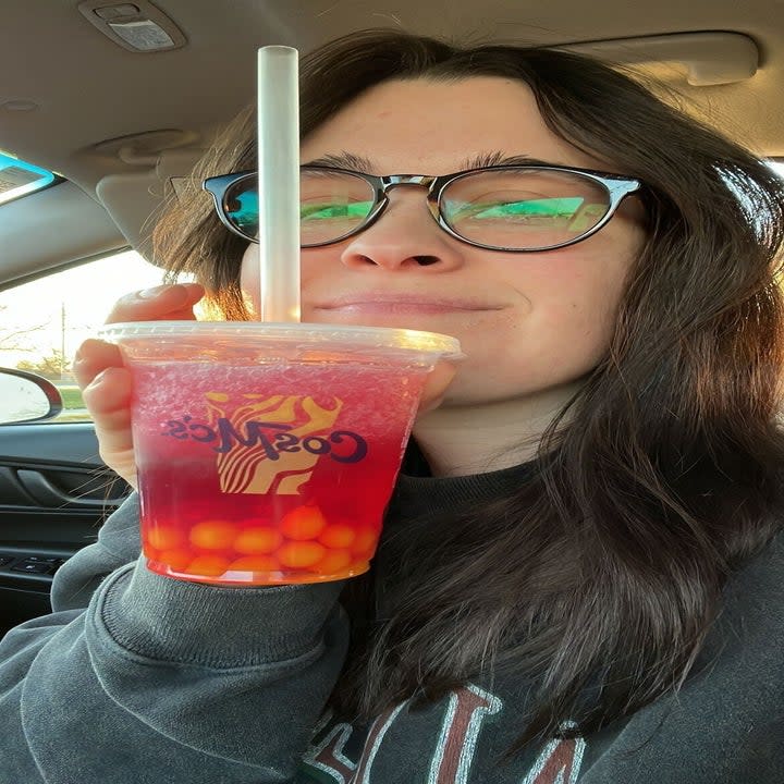 I hold a drink with boba at the bottom of the cup, and smile with no teeth showing.