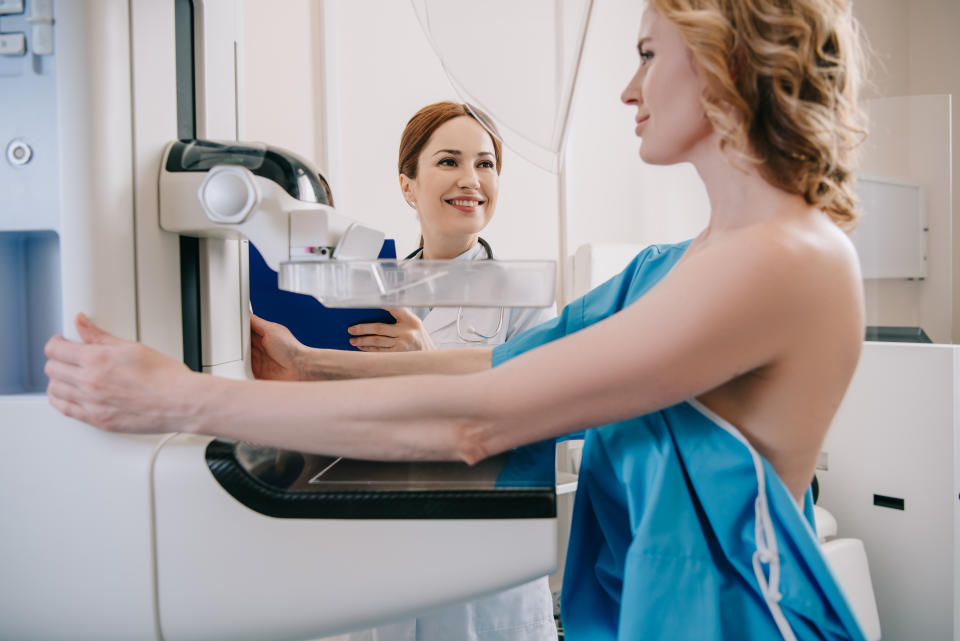 smiling radiologist standing near patient while making mammography diagnostics on x-ray machine