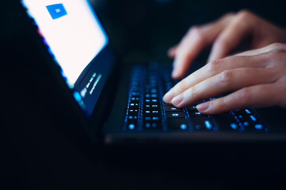  Close up hands of female using laptop in the dark at night, logging in to her online banking account to manage banking and financial bills. 