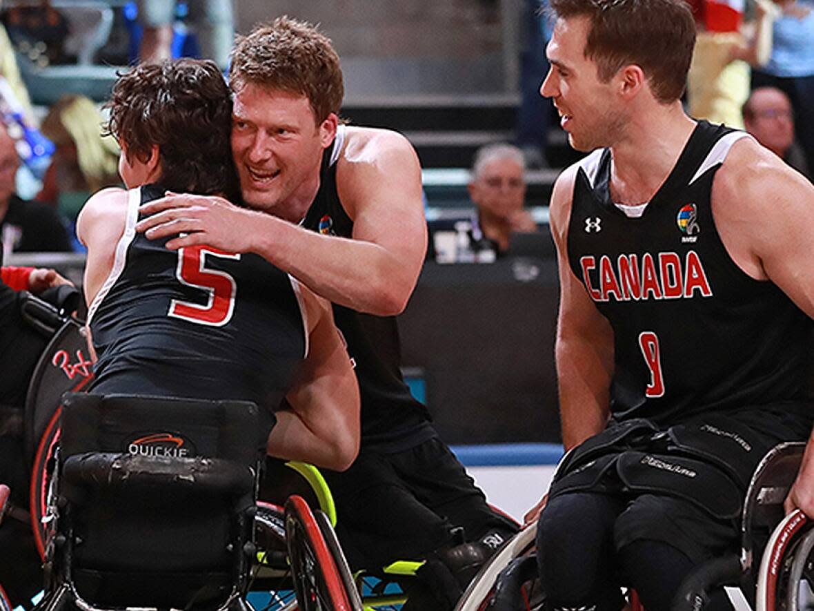 Veteran player Patrick Anderson, second from left, hugs Garrett Ostepchuk while Colin Higgins looks on following a 72-60 victory over Italy on Monday clinches a spot for Canada in the men's wheelchair basketball tournament at the Paris Paralympics this summer. (Gregory Picout/Federation Francaise Handisport - image credit)