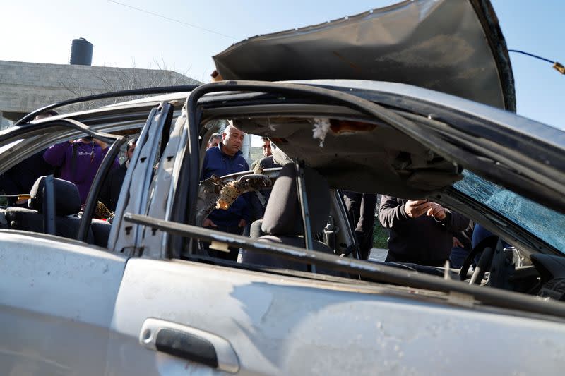 People check a damaged car where three Palestinian militants were killed during an Israeli operation, near Jenin