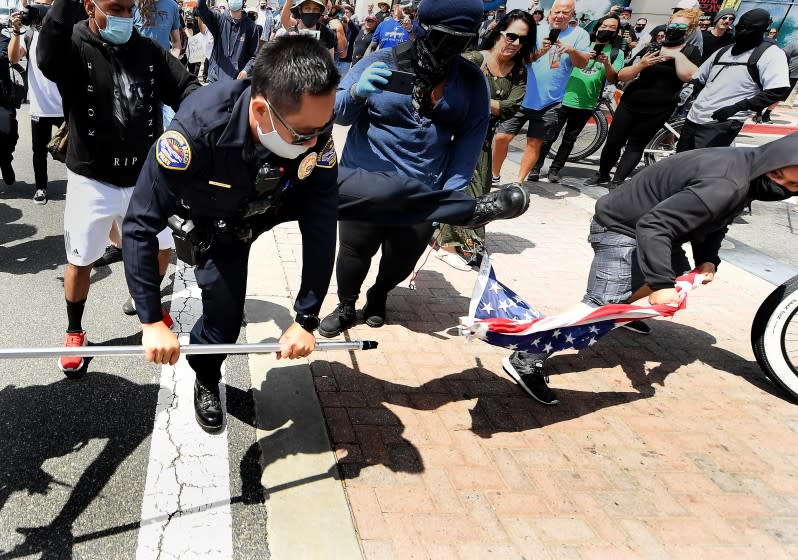 HUNTINGTON BEACH, CALIFORNIA APRIL 11, 2021-A young man steals an American flag from a White Lives Matter supporter as a Huntongton Beach police officer tries to stop it during a Black Lives Matter and White Lives Matter rally in Huntington Beach Sunday.(Wally Skalij/Los Angeles Times)