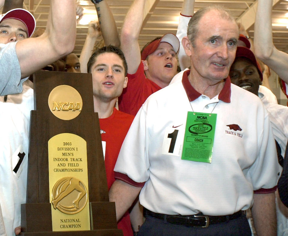 FILE - Arkansas track coach John McDonnell, right, accepts the NCAA 2003 Division I Men's Indoor Track and Field Championship trophy in Fayetteville, Ark., in this March 15, 2003, file photo. John McDonnell, the track and field coach who set a gold standard for excellence at Arkansas during his 36 years at the school, has died. He was 82. He died Monday night, June 7, 2021, according to a family statement released by the university. (AP Photo/April L. Brown, File)
