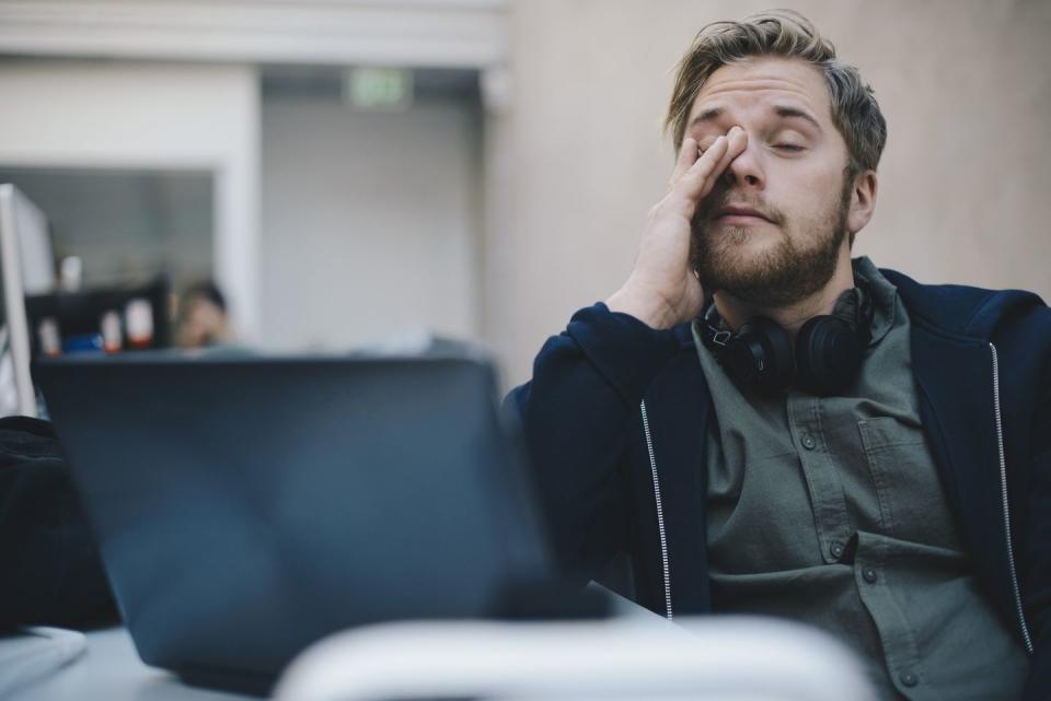 tired computer programmer rubbing eyes while sitting in office