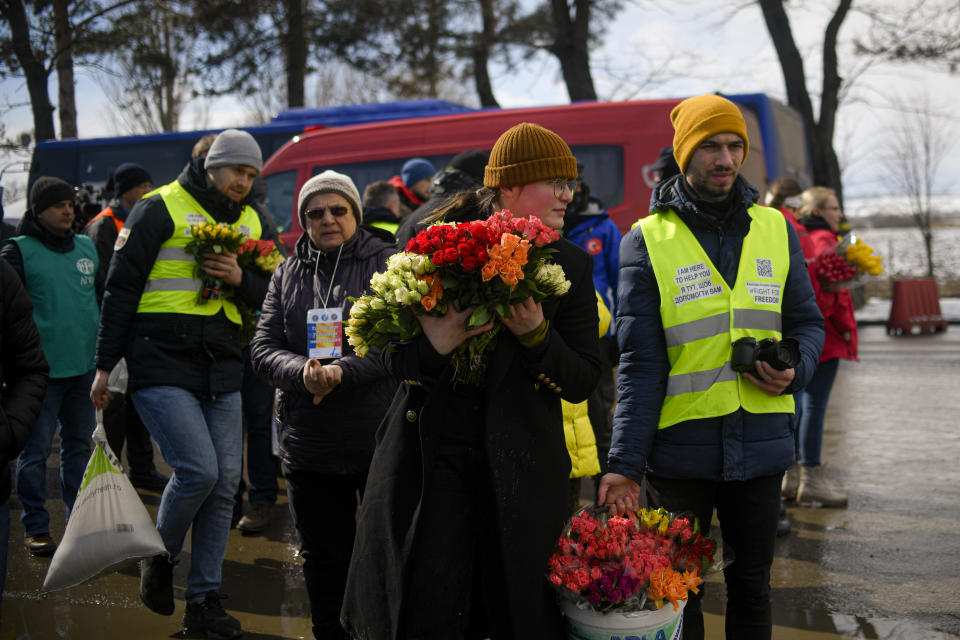 Volunteers hold flowers to give to women fleeing the conflict from neighbouring Ukraine on International Women's Day, at the Romanian-Ukrainian border, in Siret, Romania, Tuesday, March 8, 2022. It is a global day to celebrate women, but many fleeing Ukraine feel only the stress of finding a new life for their children as husbands, brothers and fathers stay behind to defend their country from Russia's invasion. (AP Photo/Andreea Alexandru)
